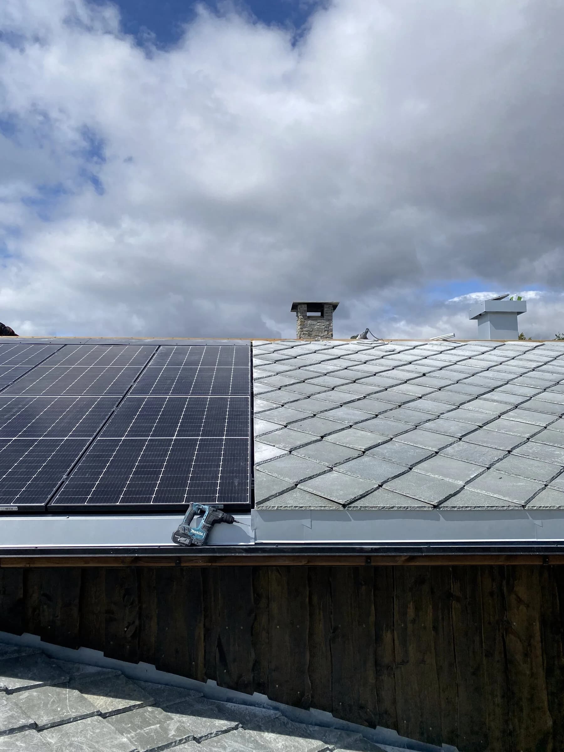 Skifertak med solcellepanel og pipe under skyhimmel